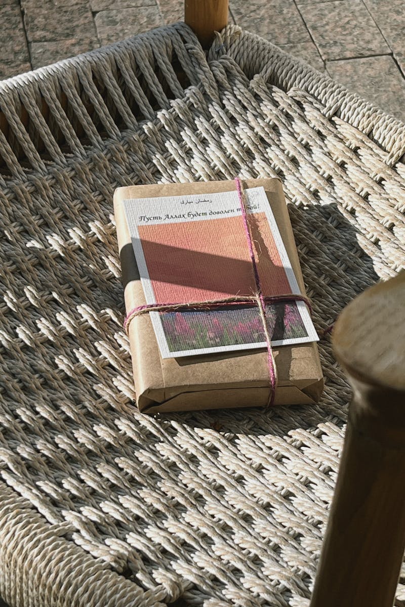 A rustic book package rests on a woven chair under warm daylight, suggesting a cozy reading nook.