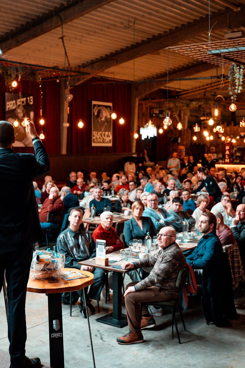A speaker addressing a large crowd in a vibrant, warmly-lit indoor venue.